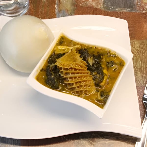 A white plate holds a mound of fufu next to a bowl of tripe and vegetable stew.