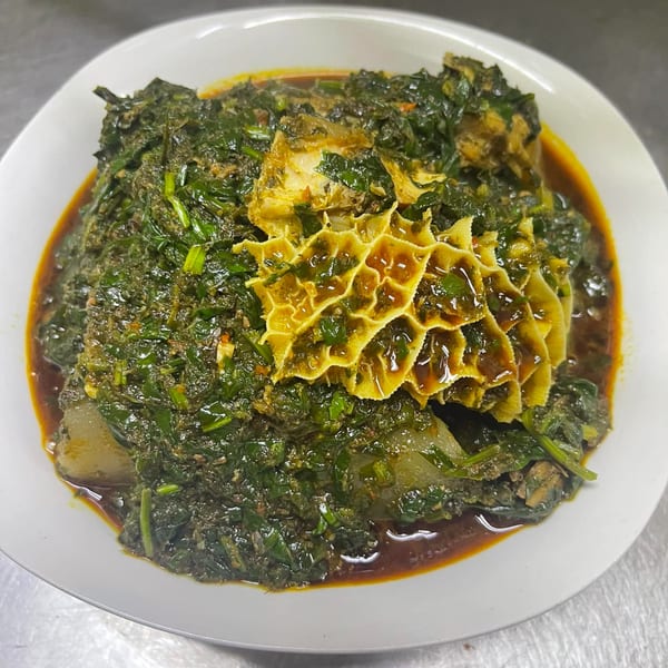 Queen Vees African Cuisine's green stew with tripe and meat in a white bowl.
