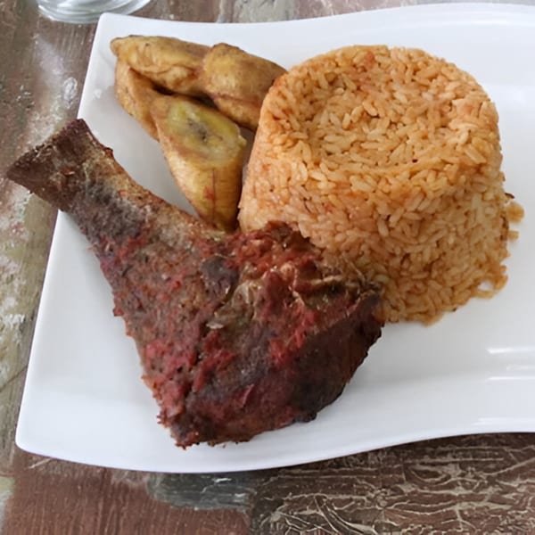 A Queen Vees African Cuisine dish with fried fish, jollof rice, and plantains on a white plate.
